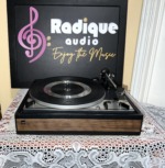 Dual 1214 turntable with the dust cover off, silver platter and tonearm on a black plinth with a walnut-grain front band