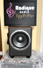 JBL Northridge E150P powered subwoofer from the front, grille off, 10 inch woofer on a grey baffle in a cherry cabinet