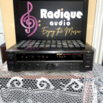JVC RX-307 stereo receiver, black front panel with power and speaker switches, bass, treble and balance dials, a large volume knob and a lit tuner display