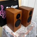 Linn Katan speakers from above and to the right, wood veneer top panels and side walls in view with the Radique Audio board leaning behind them