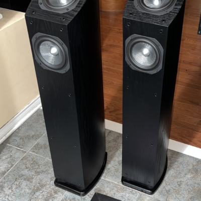 Mirage OMNI 350 towers in black ash at an angle, grilles off, standing on tile beside the Radique board