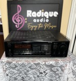 Onkyo TX-906 stereo receiver in black, front panel with display and volume knob, on lace in front of the Radique board