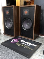 Original Large Advent speakers angled to the right with grilles off, walnut cabinets, tweeter plate set above the woofer on each baffle
