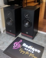 PSB 50 MkII speakers at an angle, grilles off, showing the black ash cabinets, drivers and red base trim