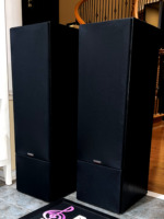Paradigm 11se Mk II towers with black grille cloths fitted, angled view showing the plain fabric fronts and the flat cabinet tops