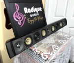 Paradigm Millenia 20 LCR speaker in gloss black at an angle, grille off, showing dome tweeters and yellow-cone woofers along the baffle