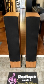 Paradigm Monitor 7 v2 towers straight on with black grilles fitted over the drivers, light cherry cabinet bases showing