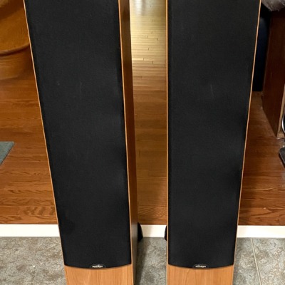 Paradigm Monitor 7 v2 towers straight on with black grilles fitted over the drivers, light cherry cabinet bases showing