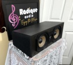 Angled view of the Paradigm Studio CC v2 center channel, grille off, showing the black cabinet side and its two woofers and tweeter