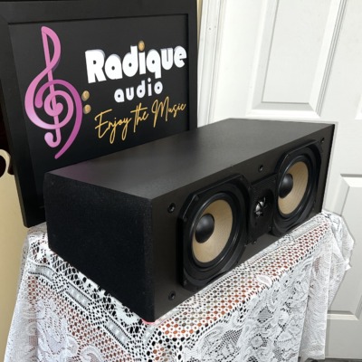 Angled view of the Paradigm Studio CC v2 center channel, grille off, showing the black cabinet side and its two woofers and tweeter