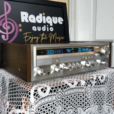 Pioneer SX-3700 stereo receiver seen from the left, brushed silver faceplate with blue-lit tuning dial set in a wood-grain cabinet