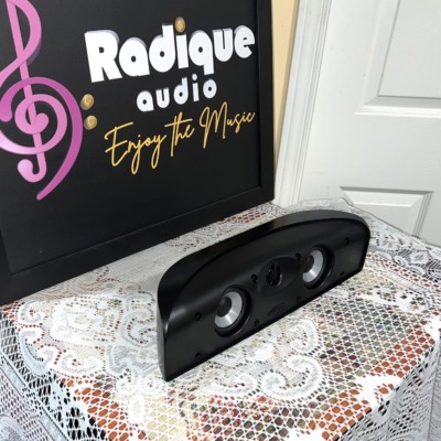 Polk Audio TL1 centre speaker in gloss black at an angle, grille off, on lace by the Radique board