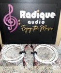 Pair of Radique House Quad speaker cables coiled on the lace table, white four-conductor jacket with red and black banana-plug tails and branded velcro wraps