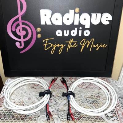 Pair of Radique House Quad speaker cables coiled on the lace table, white four-conductor jacket with red and black banana-plug tails and branded velcro wraps