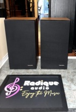 Realistic Optimus-21 speaker pair straight on with black cloth grilles fitted and the Realistic badge on each grille