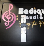 Silver Rotel RR-AT94 remote handset standing against the Radique board, numeric keypad above source, band and tone control rows