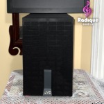 JVC SX-PW33 subwoofer standing upright, its tall narrow grille fitted with the JVC badge at the foot.