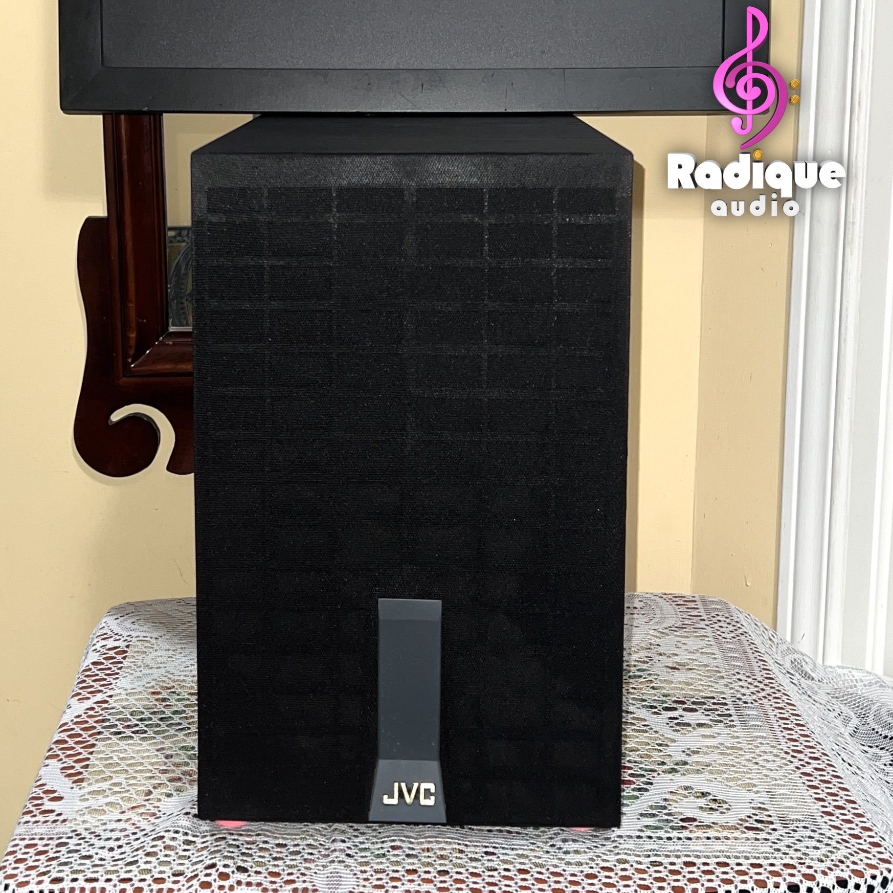 JVC-SX-PW33-1-Thumb-Logo JVC SX-PW33 subwoofer standing upright, its tall narrow grille fitted with the JVC badge at the foot.