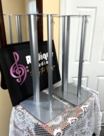 Pair of silver Linn Katan dedicated speaker stands seen from the front, each with one thick and one slim column, a shaped top plate and a broad base