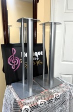 Linn Katan speaker stands in silver at an angle, showing the shaped top plates, twin columns and wide base plates resting on pink felt pads