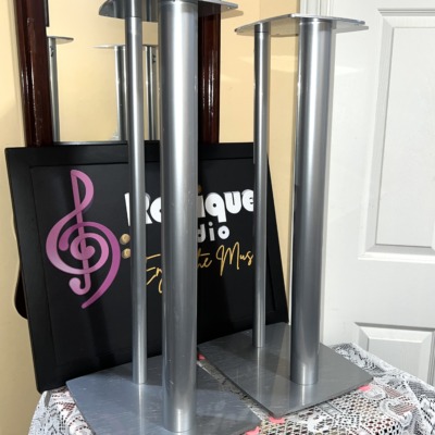 Linn Katan speaker stands in silver at an angle, showing the shaped top plates, twin columns and wide base plates resting on pink felt pads