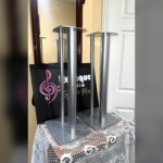 Linn Katan speaker stands in silver at an angle, showing the shaped top plates, twin columns and wide base plates resting on pink felt pads