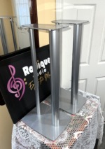 Silver Linn Katan stands from the side, one behind the other, showing the slim column's cable eyelet, the top plates and the broad bases