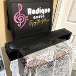 One Monitor Audio Radius 250HD with its grille fitted, lying horizontal, angled to show the curved gloss black cabinet