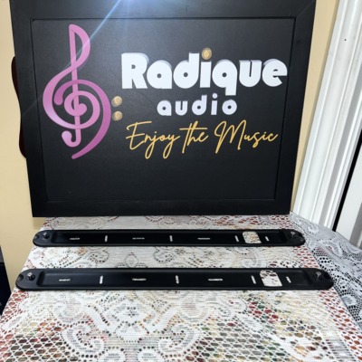 Two Monitor Audio Radius 250HD wall brackets side by side, slim black metal rails with slots for the wall screws and a stand-off at each end