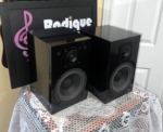 NHT Model 1C bookshelf speakers seen from a front angle, gloss black cabinets with grilles off