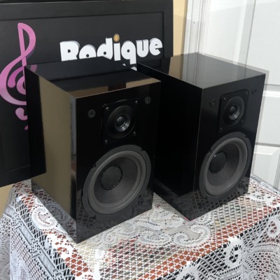 NHT Model 1C bookshelf speakers seen from a front angle, gloss black cabinets with grilles off