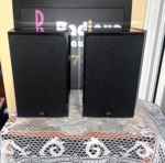 NHT Model 1C bookshelf speakers with black cloth grilles on and the NHT badge at the bottom of each grille