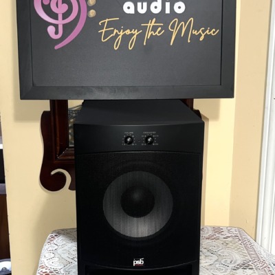PSB Alpha SubZero i subwoofer with its perforated metal grille fitted, PSB logo at the base and volume and crossover dials above