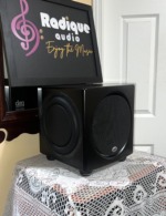 PSB SubSeries HD10 subwoofer corner view showing the front mesh grille and a passive radiator on the side of the satin black cabinet