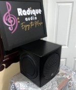 PSB SubSeries HD10 powered subwoofer from a high angle, showing the satin black cabinet top, the front grille and a side passive radiator