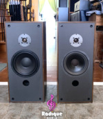 Paisley Reference Two speakers side by side with grilles off, dark wood-grain cabinets, dome tweeters, woofers and front bass ports