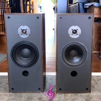 Paisley Reference Two speakers side by side with grilles off, dark wood-grain cabinets, dome tweeters, woofers and front bass ports