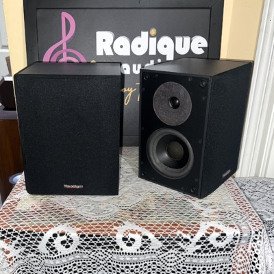 Paradigm ADP-150 surround speakers side by side, one with its black cloth grille fitted and one bare showing the tweeter and woofer