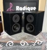Paradigm ADP-150 surround speakers in black with grilles off, angled dipole baffles each showing a tweeter above a woofer