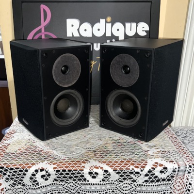 Paradigm ADP-150 surround speakers in black with grilles off, angled dipole baffles each showing a tweeter above a woofer