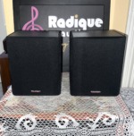 Paradigm ADP-150 surround speakers with black cloth grilles on, Paradigm logo badge at the lower corner of each grille