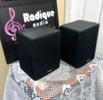 Angled view of the Paradigm ADP-150 surround pair with grilles on, showing the angled dipole cabinet shape in black