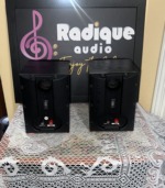 Rear of the Paradigm Micro v.3 pair showing the round bass port, wall bracket label and red and black binding posts