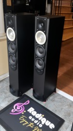 Paradigm Monitor 7 v.6 towers seen at an angle with grilles off, showing the black side panels, front drivers and outrigger feet