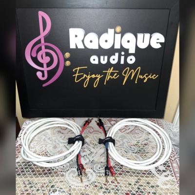 Pair of Radique House Quad speaker cables coiled on the lace table, white four-conductor jacket with red and black banana-plug tails and branded velcro wraps