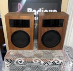 Realistic Minimus-5 speaker pair head-on, wood-grain cabinets with a black horn tweeter above a round perforated woofer grille and Realistic script badge