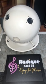 SoundSphere 2212-1 sphere turned to show its round access opening and two tweeters, sitting on its white dish with the steel hanging cable
