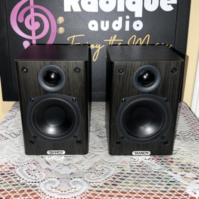 Tannoy Mercury FR Custom bookshelf speakers, dark wood-grain cabinets with grilles off showing the tweeter and black woofer