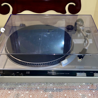 Technics SL-220 belt-drive turntable from the front with its clear dust cover closed, silver plinth and Technics control strip