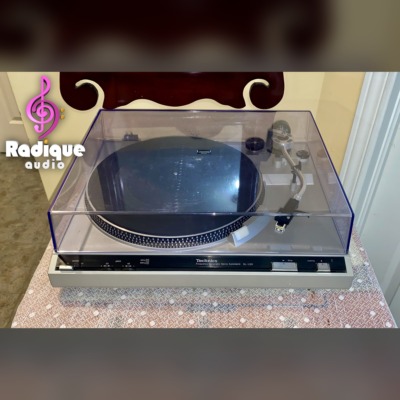 Technics SL-220 belt-drive turntable from the front with its clear dust cover closed, silver plinth and Technics control strip